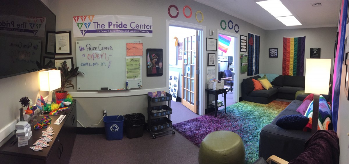 Photo of the Pride Center Lounge, which includes LGBTQ+ flags, rainbow decorations, and a sign reading "The Pride Center is Open! Come on in!"