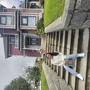 Ariel sitting in front of the red charmed house wearing light wash jeans, a beige long sleeve shirt with straightened black hair