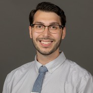Bill Burden smiling headshot from the chest up wearing a white and blue stripped shirt, light blue tie