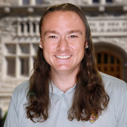 Scottie Burden with long brown hair and a gray polo with a gray building in the background
