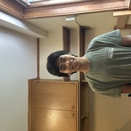 Josue is smiling at the camera while standing in their dorm room with book shelves and a desk behind her.