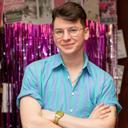 Lyam standing with his arms crossed in front of a pink shimmering backdrop