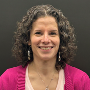 A photo of Peggy, a white woman with curly brown hair wearing a hot pink cardigan and a light pink shirt