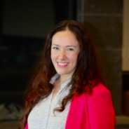 Natalie is pictures here. She is a fair-skinned woman with brown hair, wearing a white blouse, pink blazer, and pink lipstick.