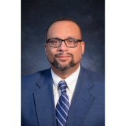 Pictured is Dr. Robinson. He is a light skinned black man with a beard in a blue suit and tie. He is wearing black frame glasses