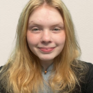 Delaina in front of a white background with a black sweater and gray undershirt